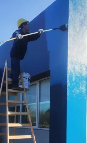 Hombre en escalera pintando pared de azul
